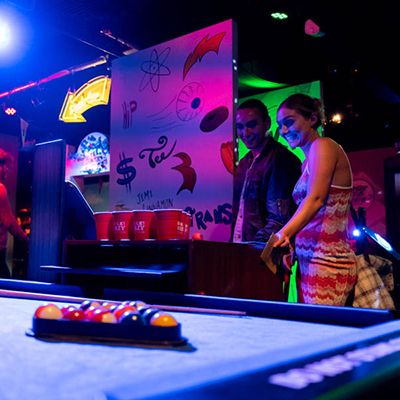 Two people playing pool at a pub in purple lighting