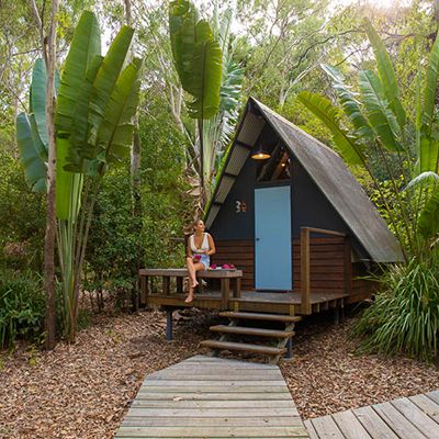 Little A-frame house in the forest with a woman sitting on the deck