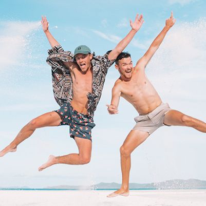 Two men jumping with their arms spread on a sandy beach