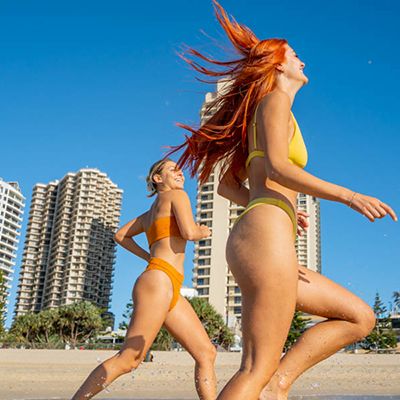 Two women running in colourful bikinis on the beach