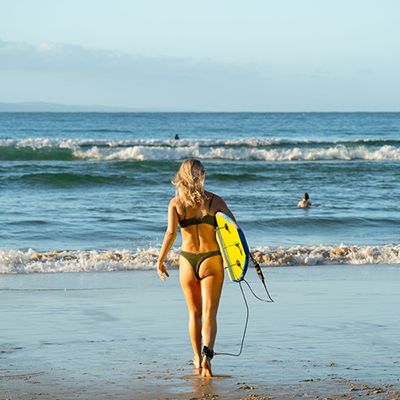 A woman walking into the water with a surfboard in Byron
