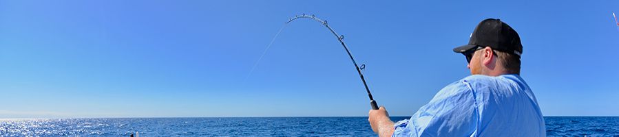 Man wearing a cap reeling in a fish on a Whitsundays fishing charter