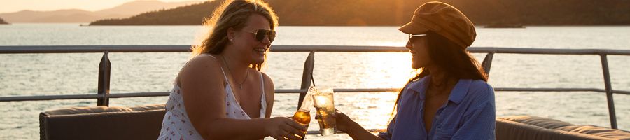 girls clinking drinks on the deck of a boat at sunset