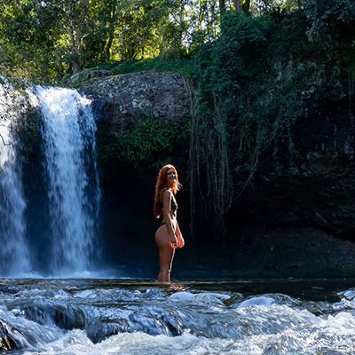 A woman standing in the sunlight next to a waterfall