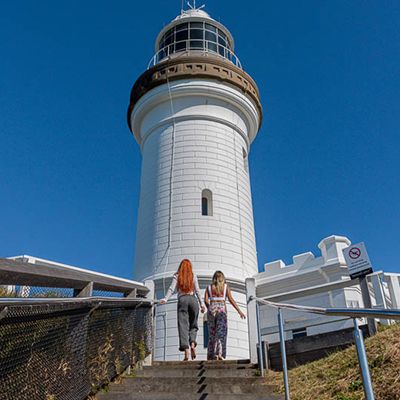 Two people walking up to the Byron Bay Lighthouse on a sunny day