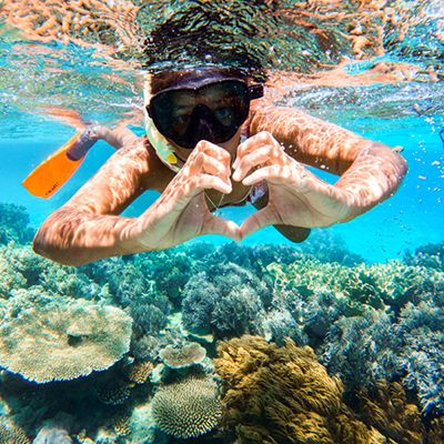 A person snorkelling the Great Barrier Reef with a love heart sign with hands