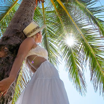 Woman in a hat standing in front of palm trees in a white dress