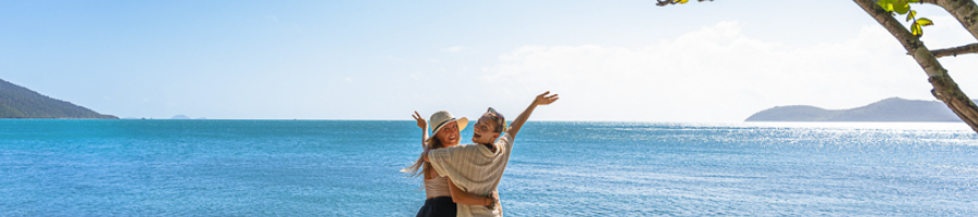 Two girls standing in front of a beach but looking at the camera