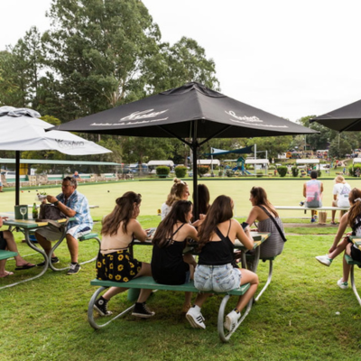 People sitting at tables under shade umbrellas next to bowling green