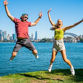 Two backpackers jumping and smiling in front of the Sydney Harbour Bridge