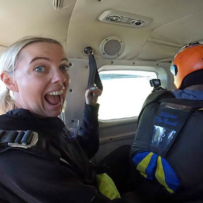 A woman smiling with blonde hair in gear with a tandem skydiver