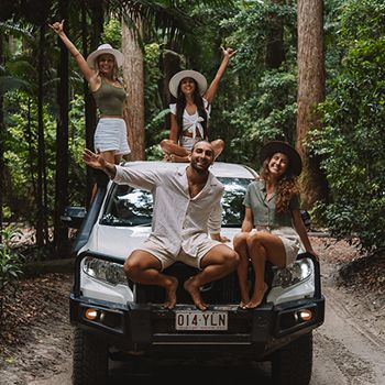 Group of travellers on a 4WD in neautral tones in big green forest setting smiling