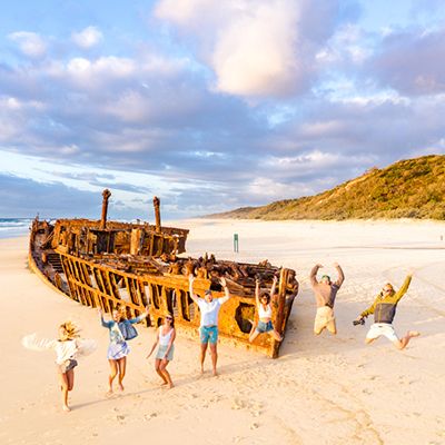 people jumping in front of shipwreck on the beach