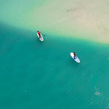 Two people on Stand Up Paddle-boards in bright blue water