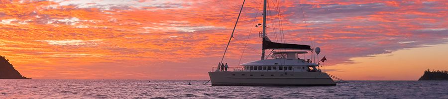 catamaran sailing in front of a pink sunset at sea