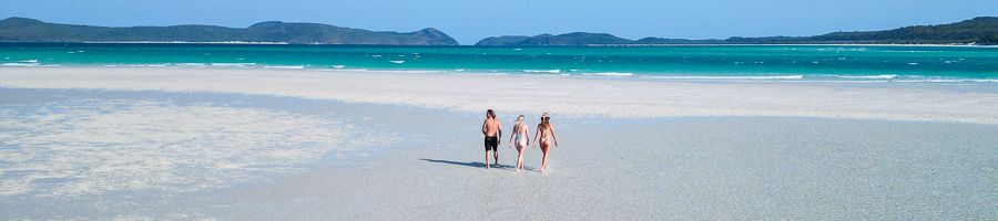 three travellers walking on white sand beach in the whitsundays