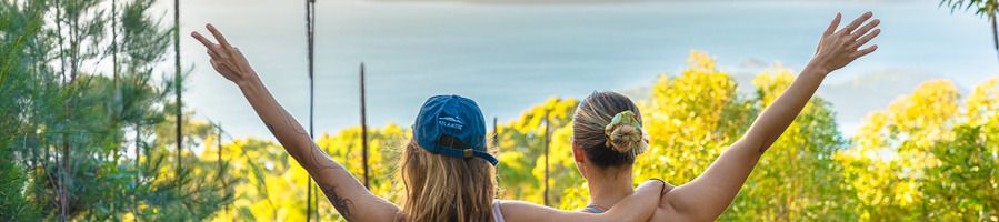 Two girls at the end of a bushwalk, looking out at an island in the Whitsundays