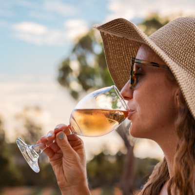 Woman sipping wine from wine glass wearing sunglasses and a hat