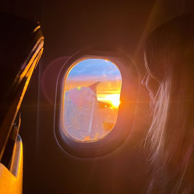 girl gazing out the window of an airplane at sunrise