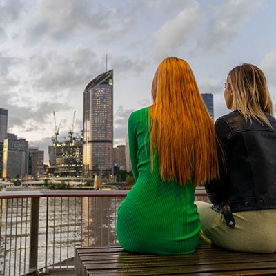 girls sitting by the water looking at Brisbane CBD