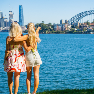 Two women standing on Sydney shoreline looking Harbour Bridge