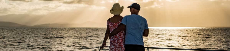 Couple standing on bow of sunset sailing catamaran