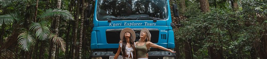 two girls posing in front of kgari explorer tours bus