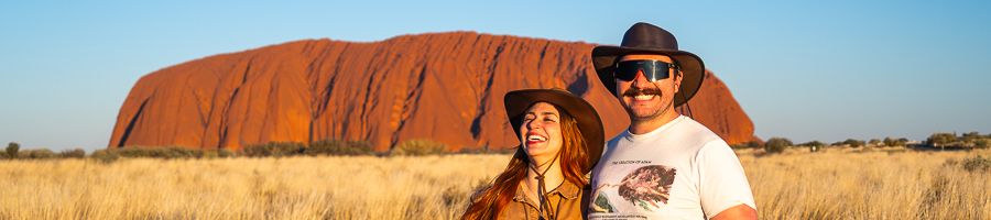 couple smiling in front fo uluru in the red centre