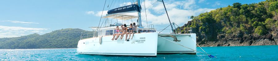 White catamaran in the Whitsundays with people on the deck sitting