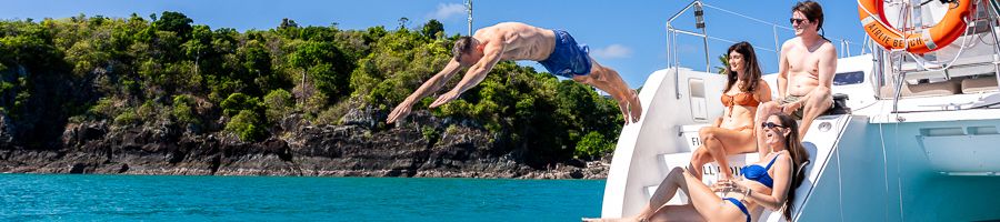 A man diving off a catamaran while others watch and smile