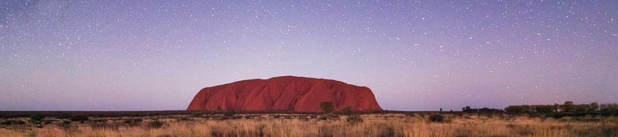 uluru monolith with purple starry sky behind