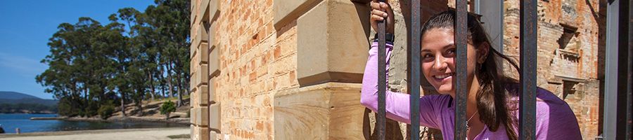 A woman in a pink shirt holding onto the bars of old prison 