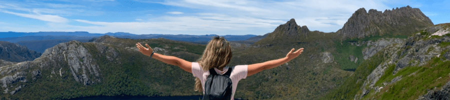 The back of a woman with long hair standing on a mountain looking at more mountains