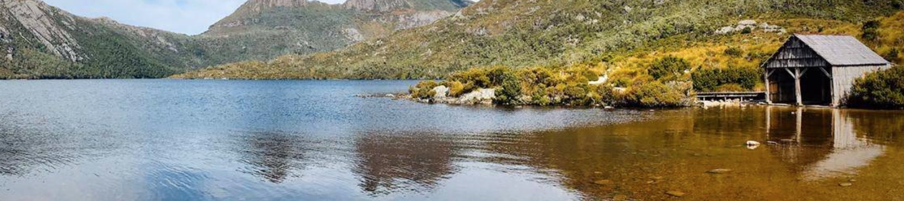 A landscape photo of a hut on a lake with mountains behind