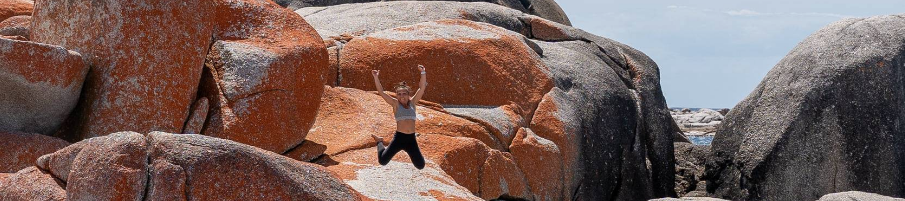 A woman jumping in front of an orange coloured rock