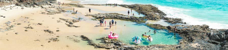 bright blue rock pools on k'gari with tourists swimming