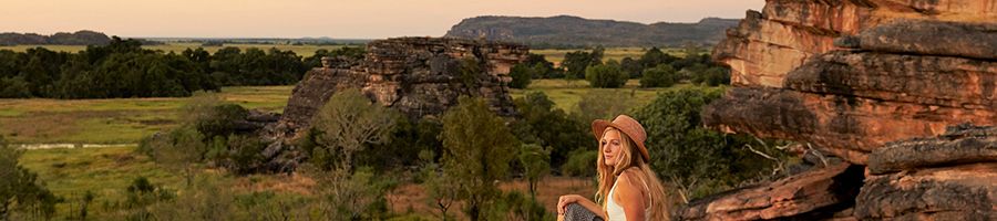 woman in a hat sitting on rocks admiring the view of kakadu national park