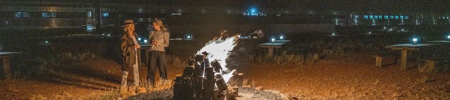 women standing by a campfire in front of the ghan train