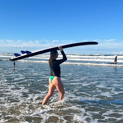 person walking in the ocean with surfboard on head