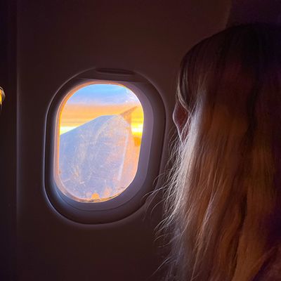 girl looking out the window on an airplane at sunrise