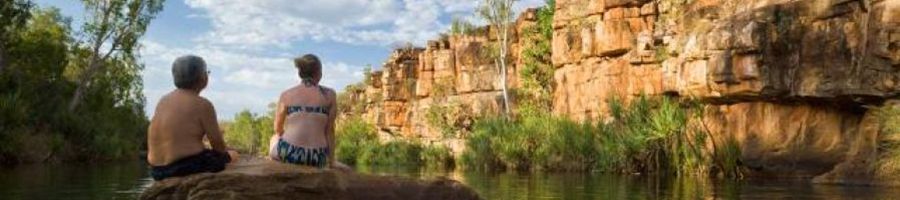 two people sitting on rocks in a rugged water hole