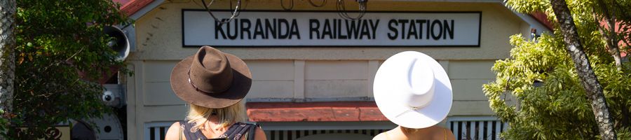 two travellers in hats standing in front of kuranda railway station