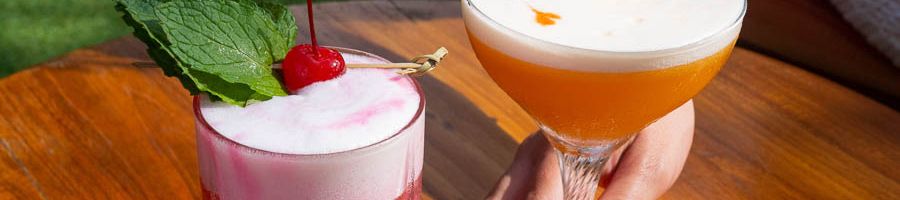 two cocktails on a wooden table at a bar