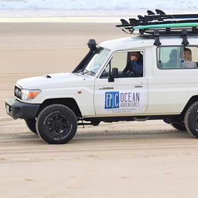 white 4wd with surfboards on top driving the beach