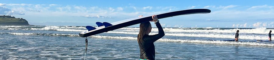 A woman holding a surfboard above her head as she walks in to the sea