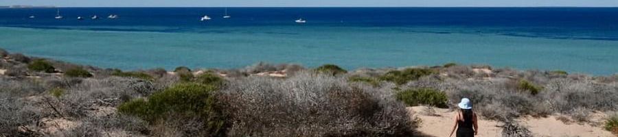 woman walking along a bright blue beach in western australia