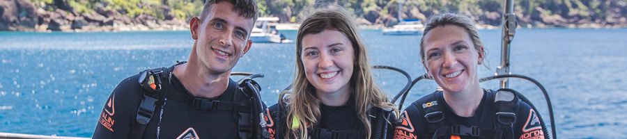 three scuba divers smiling on a boat in the whitsundays