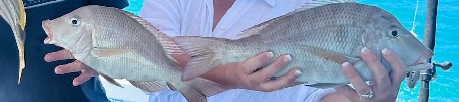 A woman holding up two fish that she caught