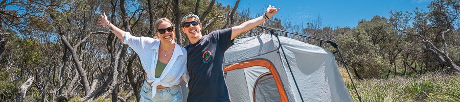 couple smiling in front of tent outside in nature