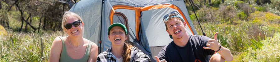 three people smiling in front of tent in the wilderness